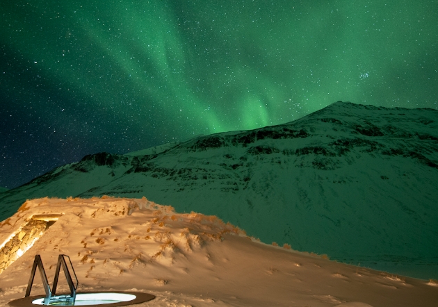 Geo-thermally heated outdoor pool at Deplar Farm in Iceland at night with the Northern lights