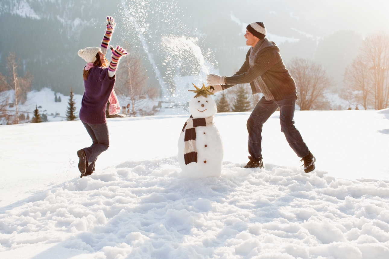 couple building a snowman wrapped up in woolly gear