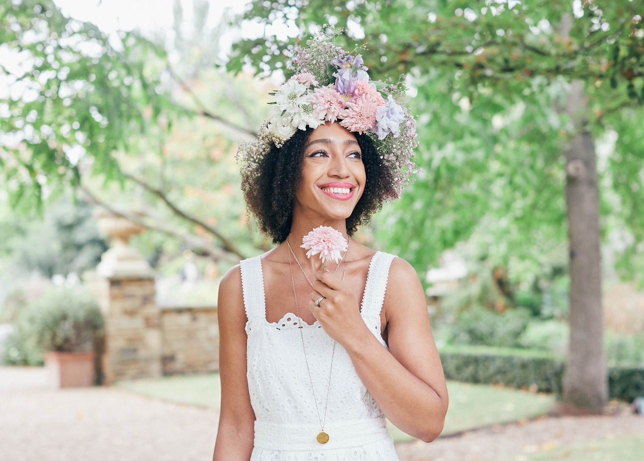 Hazel Gardiner in white dress flower crown and holding a flower