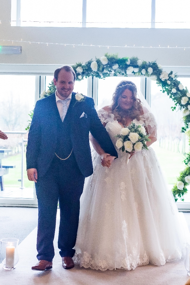 Bride and groom walk through flower arch