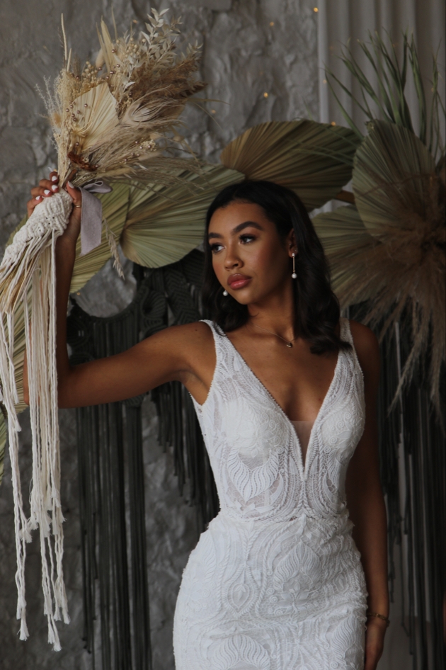 Bride in dress poses in front of plants indoors