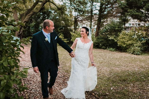 Bride and groom walk hand-in-hand up a gravel drive