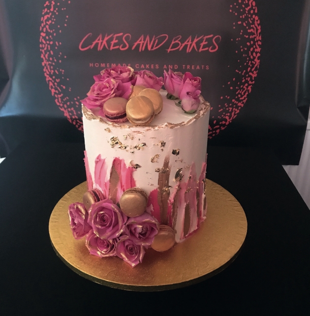 Light pink cake on gold base decorated with pink macarons and pink roses