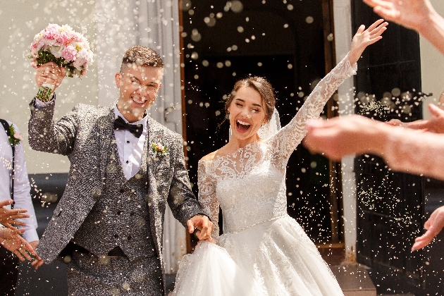 Bride and groom celebrating while their guests throw confetti