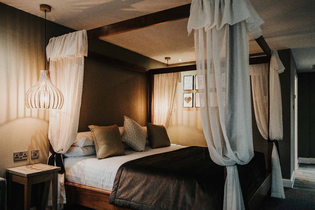 bedroom suite with four poster bed in it, voile draping, soft colour and lighting