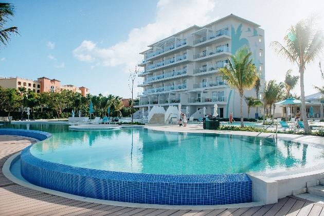 A large white building surrounded by a swimming pool, sun loungers and trees