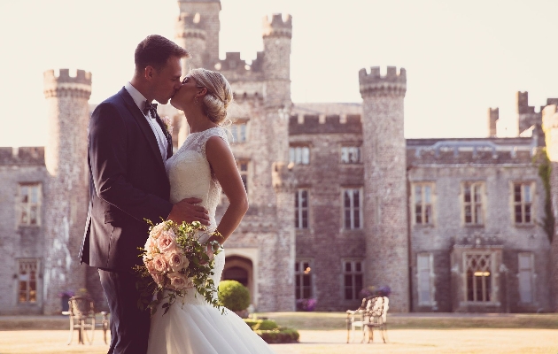 A bride and groom kissing in front of a castle