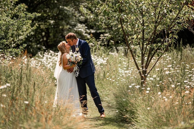 A bride and groom kissing in a field full of white flowers