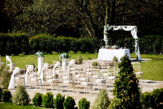An outdoor wedding ceremony with an arch at the end of the aisle