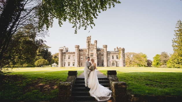 A bride and groom standing in front of a grand castle