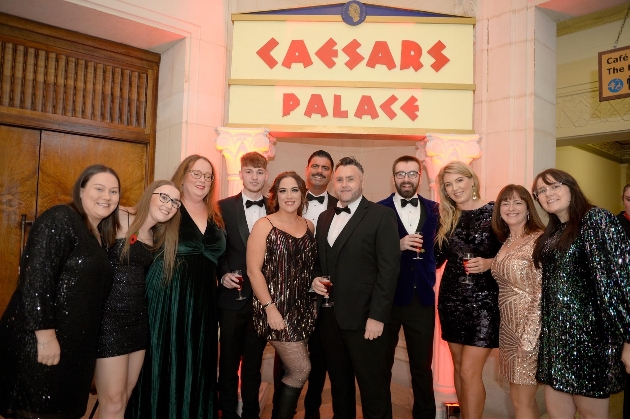 A group of men and women dressed smart under a sign that reads Caesars Palace