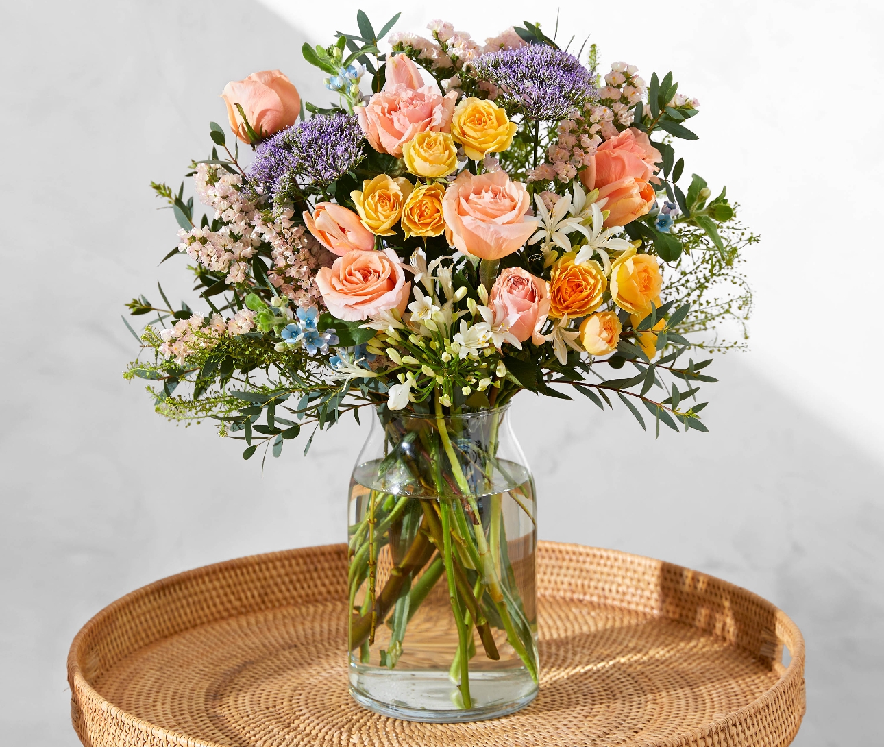 Bloom & Wild's peachy bouquet in a vase of water on a table 