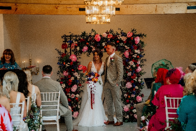 A bride and groom getting married in front of a flower arch