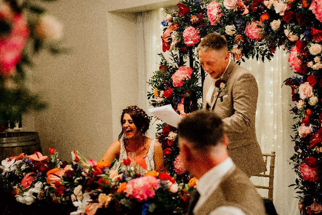 A groom reading a speech while the bride laughs