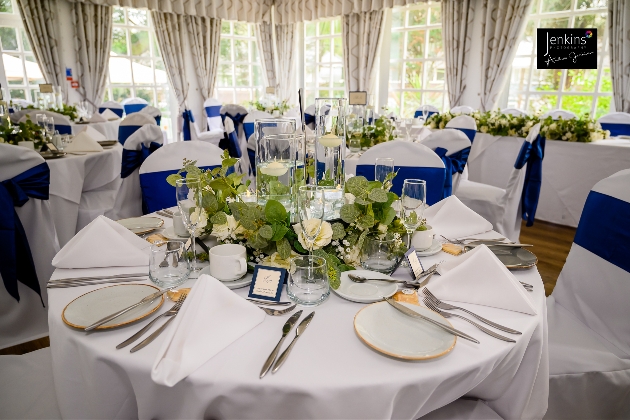 A room full of tables with white table cloths and blue chair sashes