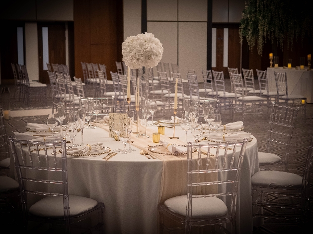 A round white table decorated with flowers and clear chairs