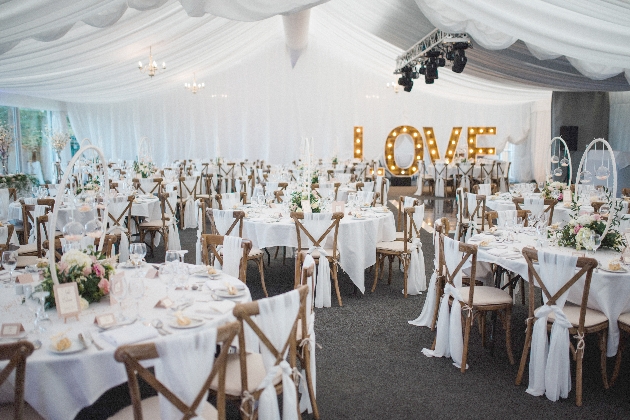 A marquee decorated with round tables and giant love letters