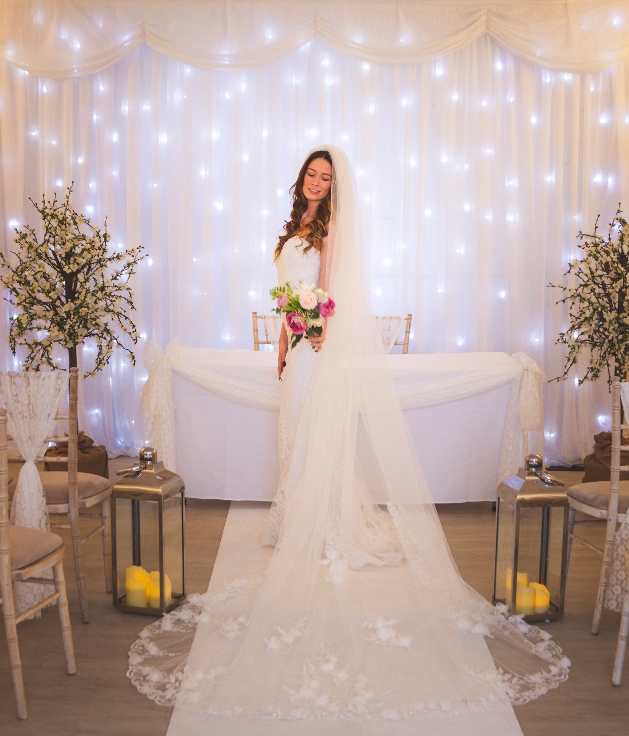 A bride standing in front of a white table and wall of fairylights
