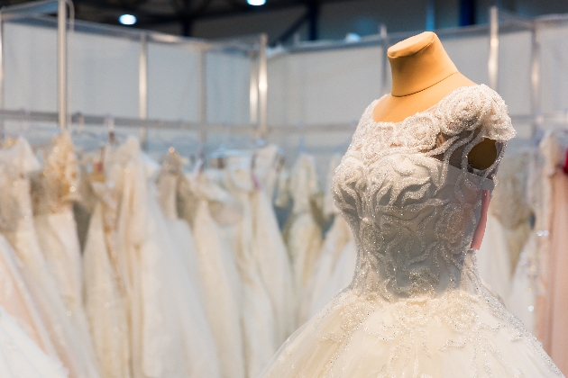 A mannequin with a wedding dress on with racks of dresses in the background