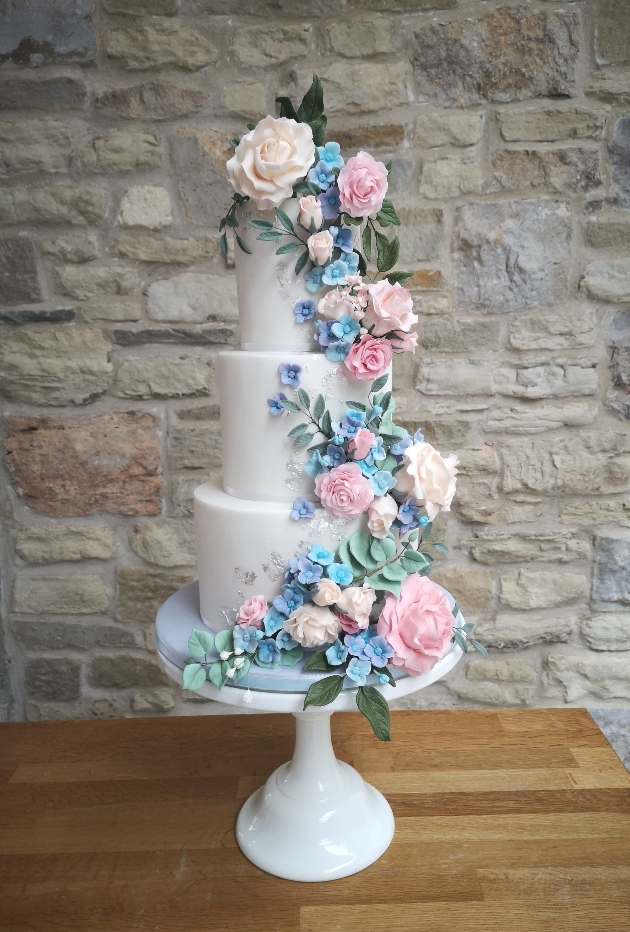 A white wedding cake covered in pastel flowers