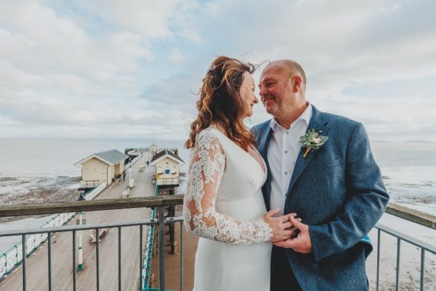 A bride and groom embracing in front of a pier