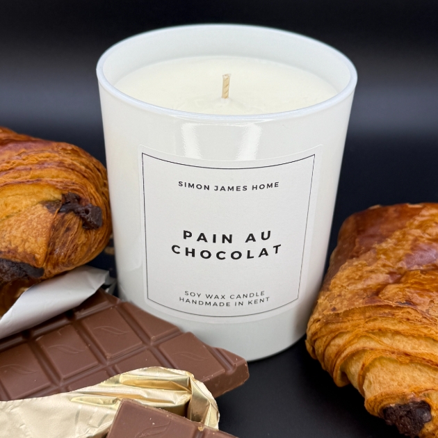 white candle labelled as Pain Au Chocolat with pastries and chocolate laying next to it