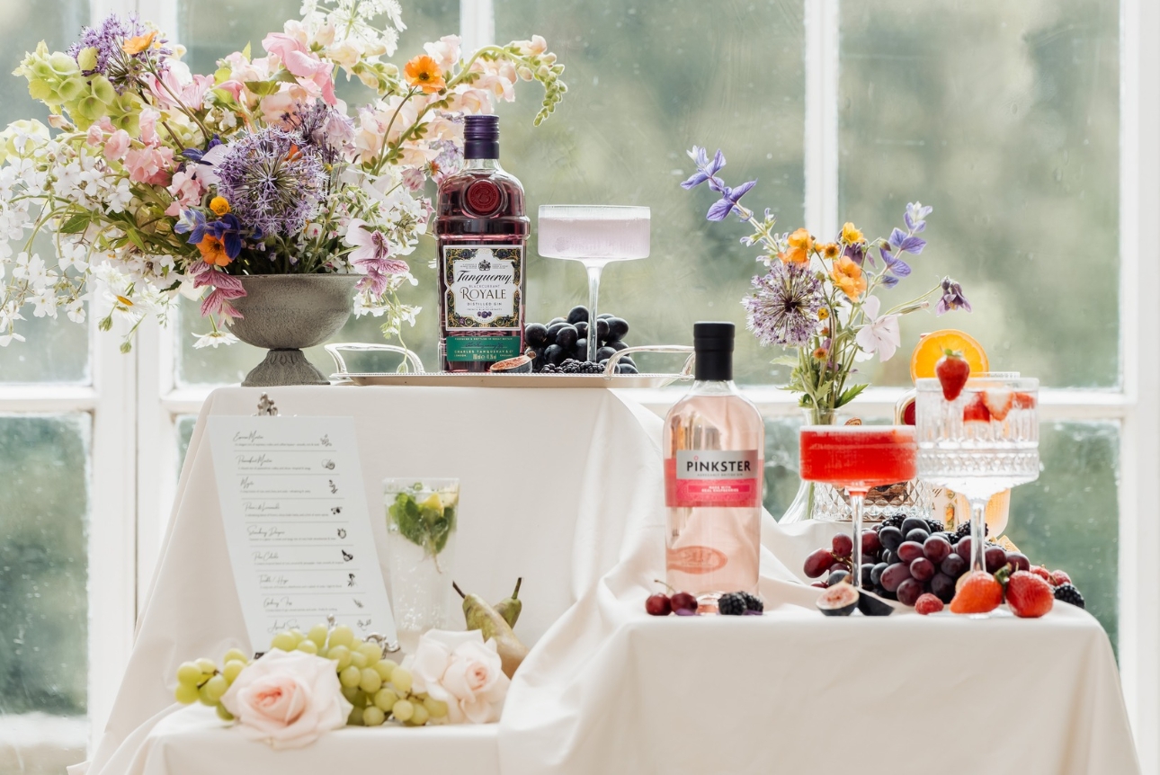 three staggered height tables set up with various cocktails, bottles and fruits
