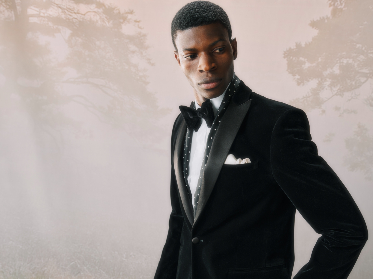 man in black suit standing in front of pink backdrop