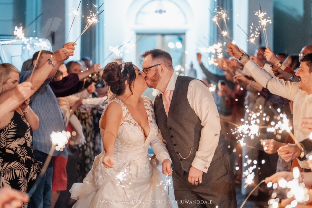 A bride and groom standing with sparklers while surrounded by friends and family