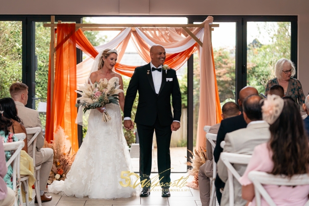 A bride and groom standing at the end of the aisle surrounded by friends and family