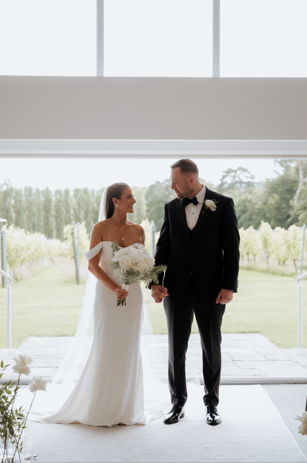 A bride and groom holding hands at the end of the aisle