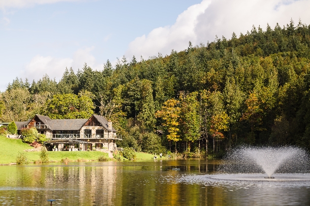 A large brick building next to a lake, fountain and forest