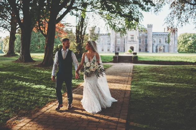 A bride and groom walking hand-in-hand with a castle in the background