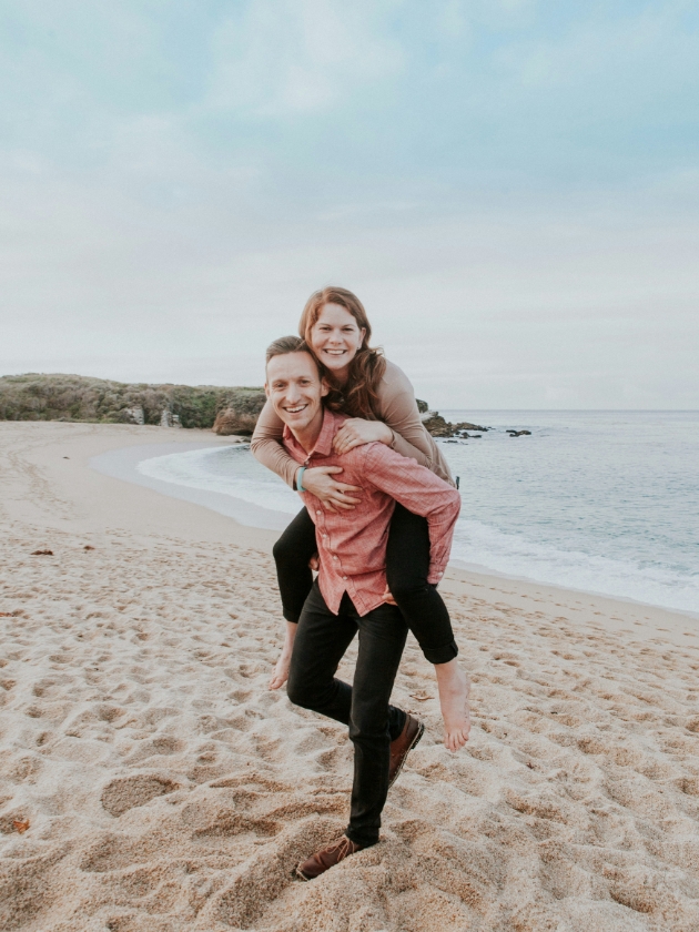 man giving woman piggy back on a beach